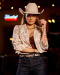 Woman wearing a cowboy hat and patterned jacket in a dimly lit room with neon signs.