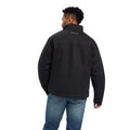 A man wearing a black Grizzly canvas jacket with a sherpa lined collar, multiple zippered pockets, and standing collar.
