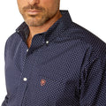 Man wearing a patterned dark shirt and dark pants on a white background