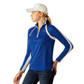 Woman wearing a blue and white long-sleeve athletic jacket with Ariat branding with a white cap on a white background