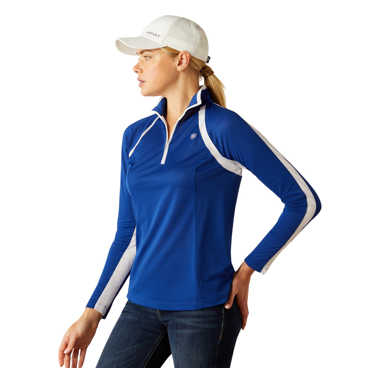 Woman wearing a blue and white long-sleeve athletic jacket with Ariat branding with a white cap on a white background
