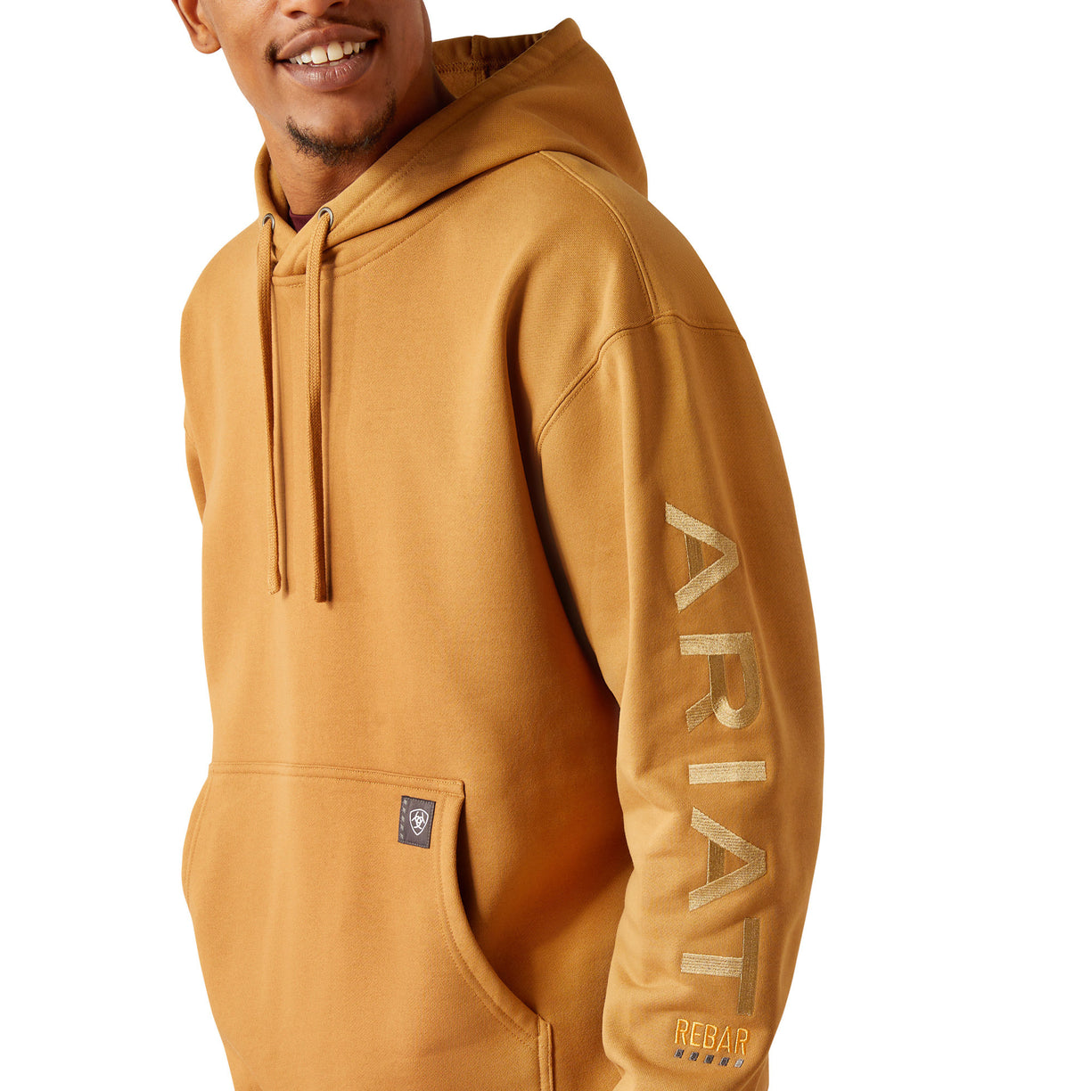 Man wearing a mustard yellow hoodie with Ariat branding on a white background