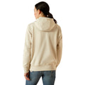 Woman wearing a beige hoodie with Ariat brand logo on a white background