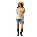 Woman wearing a beige t-shirt with floral and deer design, blue jeans, and a cowboy hat on a white background