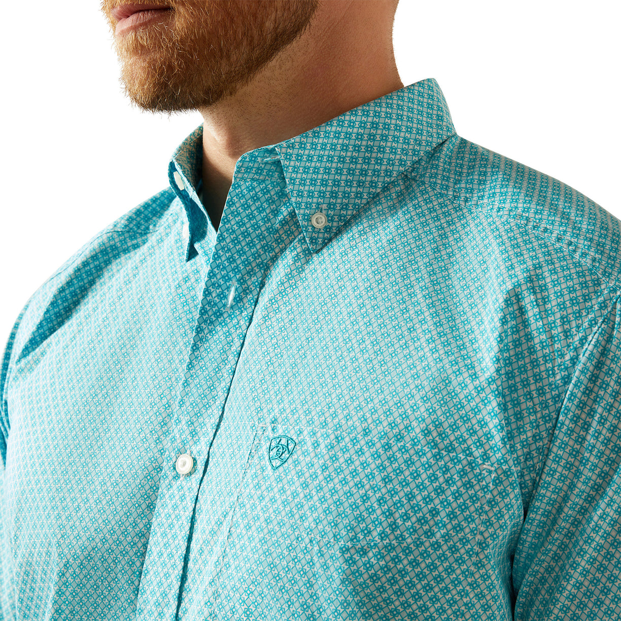 Close-up of a person wearing a turquoise patterned shirt with a brand logo.