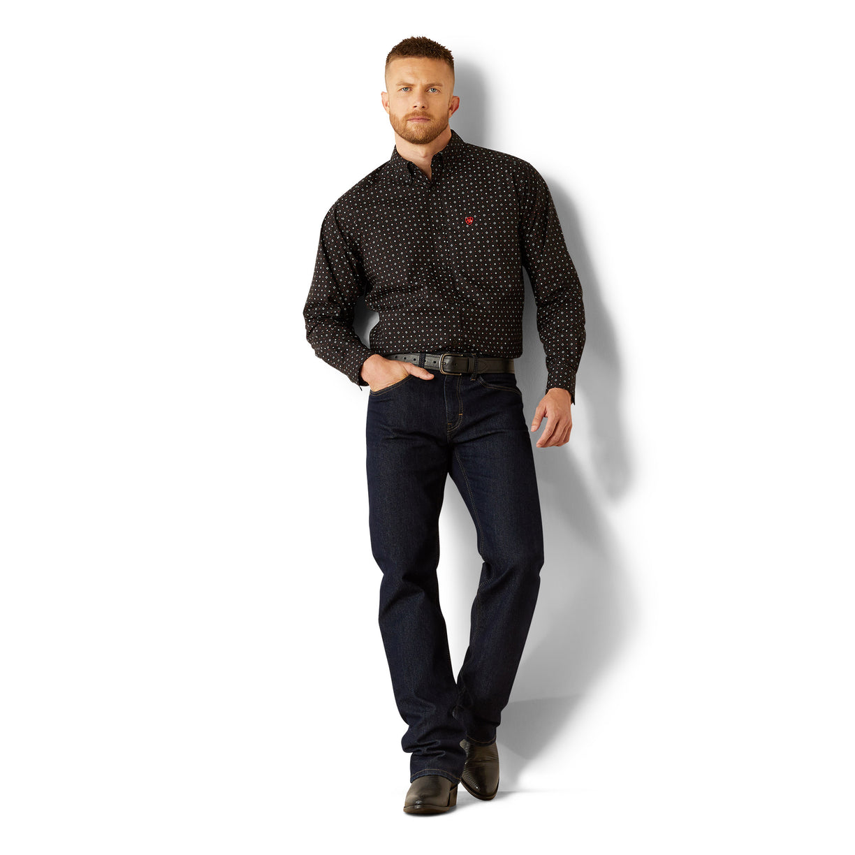 Man wearing a black patterned shirt and dark jeans on a white background