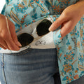 Person holding sunglasses with a floral shirt and jeans in the background