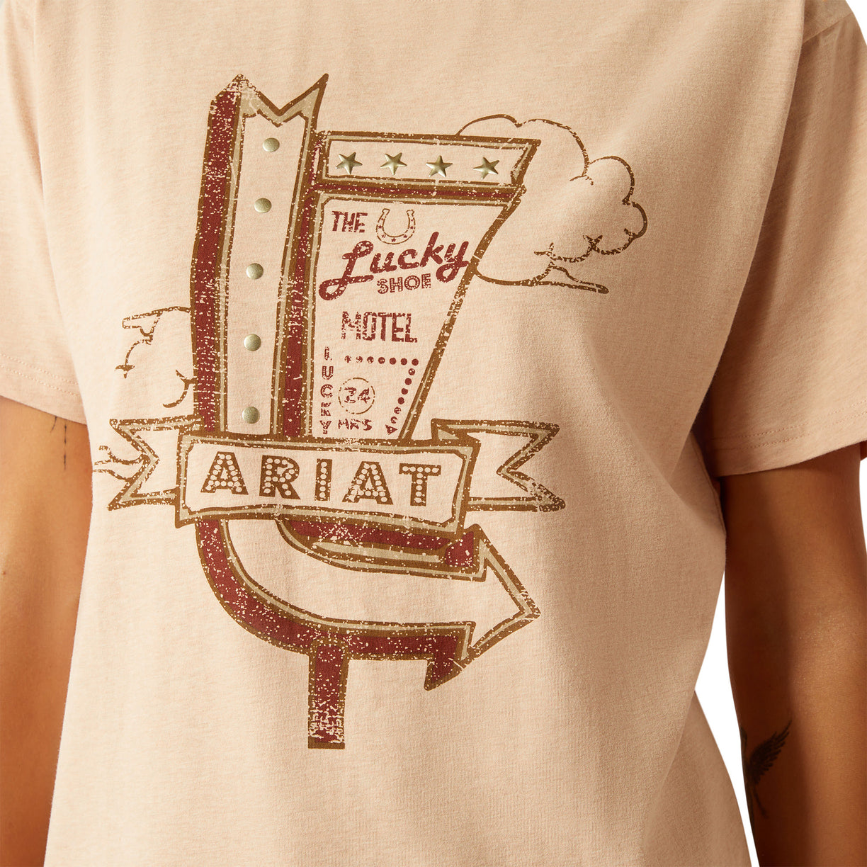 Beige t-shirt with 'Lucky Shoe Motel' graphic design on a person wearing it.