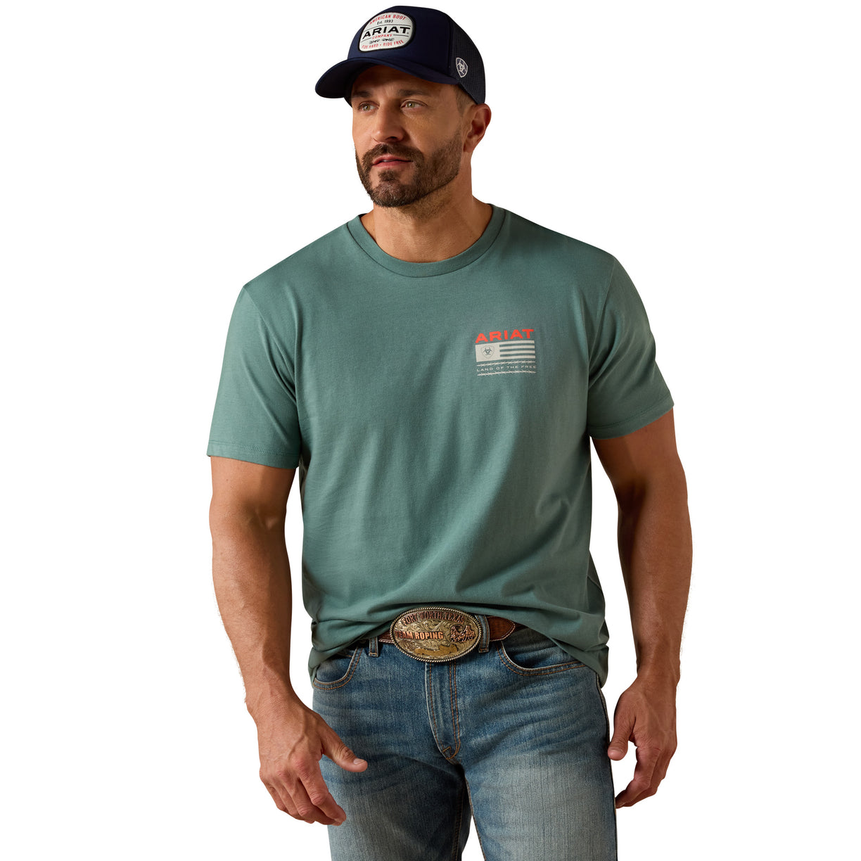 Man wearing a green t-shirt with a logo, blue jeans, and a cap on a beige background