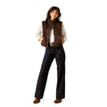 Woman wearing a brown vest, white shirt, and dark jeans on a white background