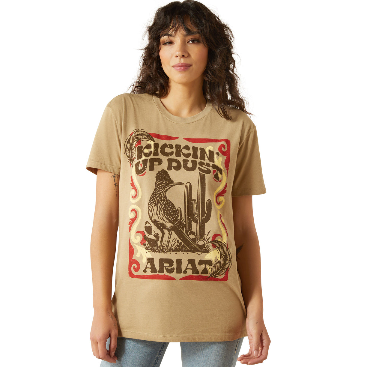 Woman wearing a tan t-shirt with a graphic design and 'Ariat' branding.