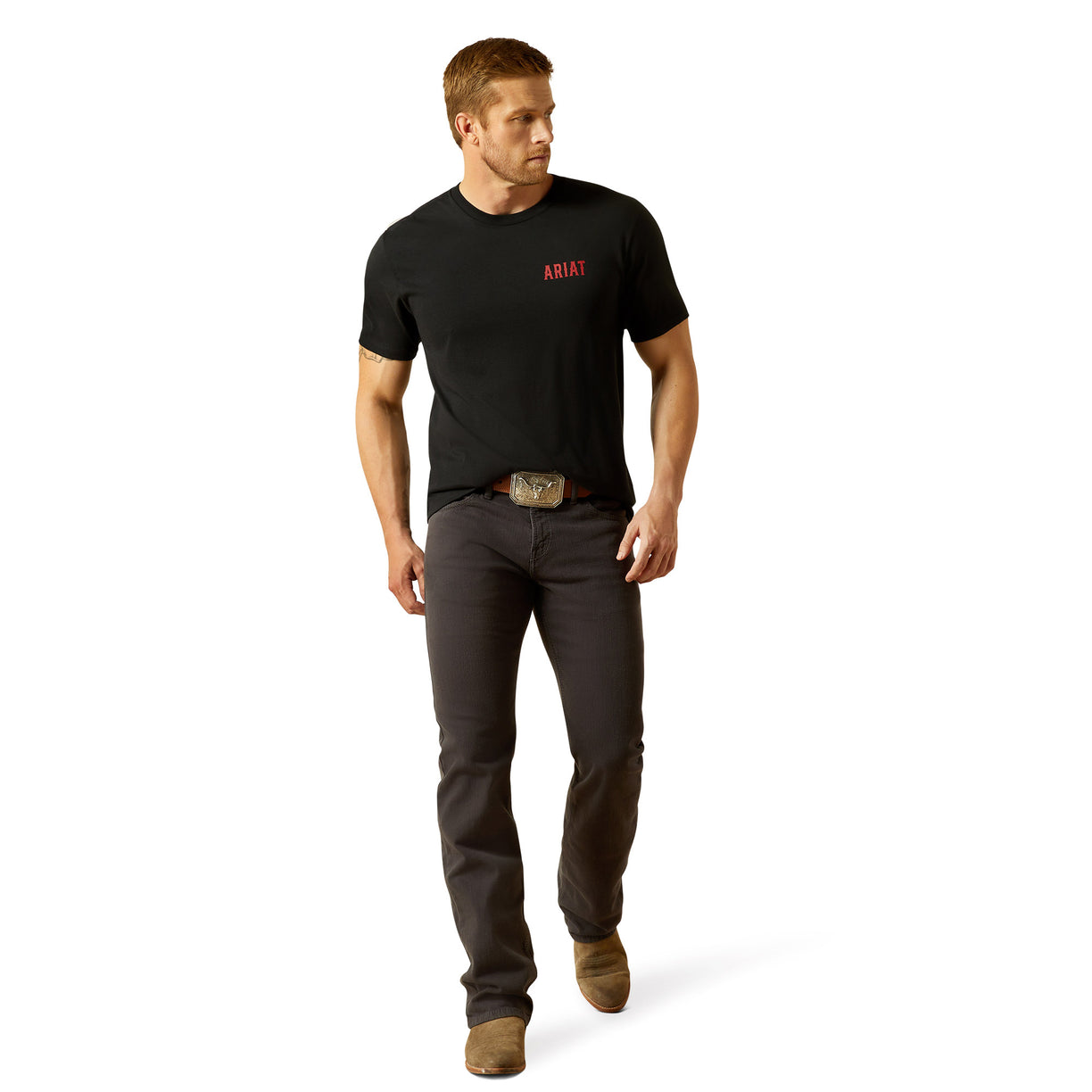Man wearing a black t-shirt with 'Ariat' logo and dark jeans on a white background