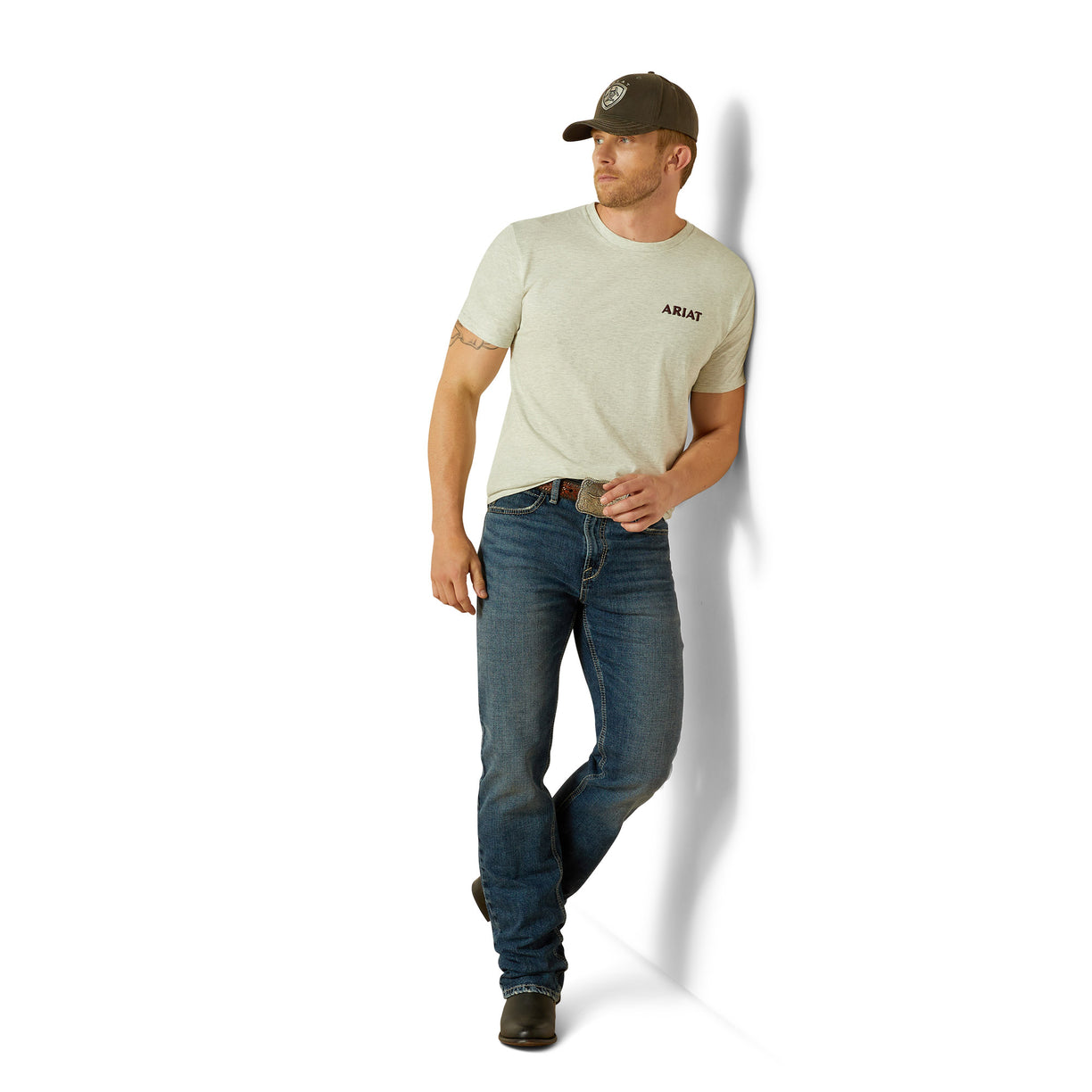 Man wearing a beige t-shirt and blue jeans with a cap, standing against a white background