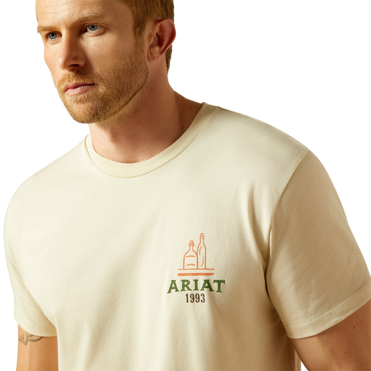 Man wearing a beige t-shirt with Ariat logo on a white background