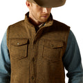 Man wearing a brown vest over a blue shirt with a white background