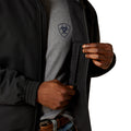 Person wearing a black jacket with a brand logo, holding the hood.