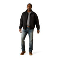 Man wearing a black jacket, gray shirt, blue jeans, and brown boots on a white background