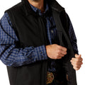 Person wearing a black vest over a blue plaid shirt with a visible brand logo.