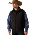 Man wearing a black vest over a plaid shirt with a cowboy hat on a beige background