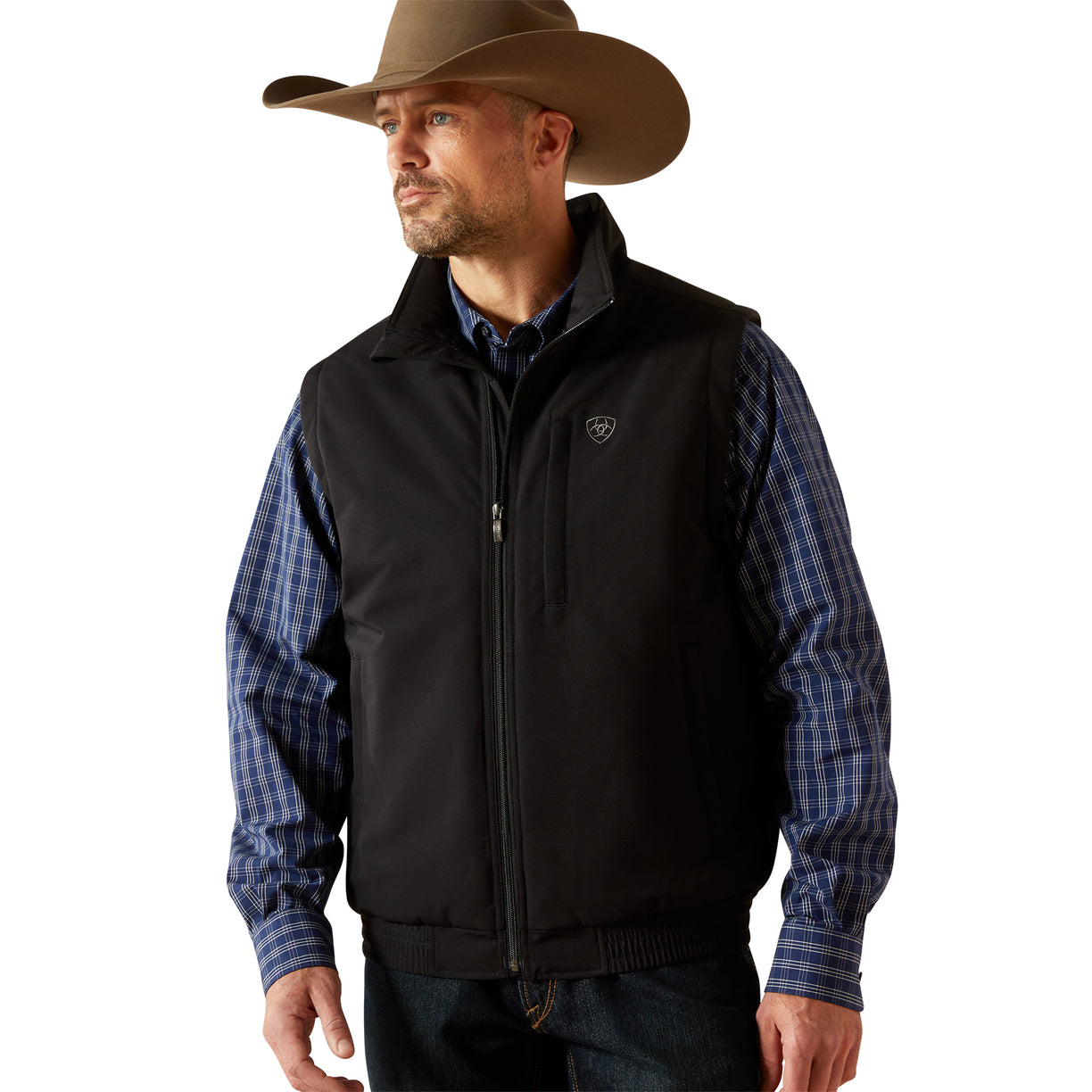 Man wearing a black vest over a plaid shirt with a cowboy hat on a beige background