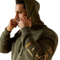 Man wearing a green hoodie with brand logos on sleeves against a white background