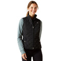 Woman wearing a black quilted vest over a light blue long-sleeve shirt on a white background
