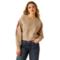 Woman wearing a beige sweater with a red design on the sleeve and blue jeans against a white background
