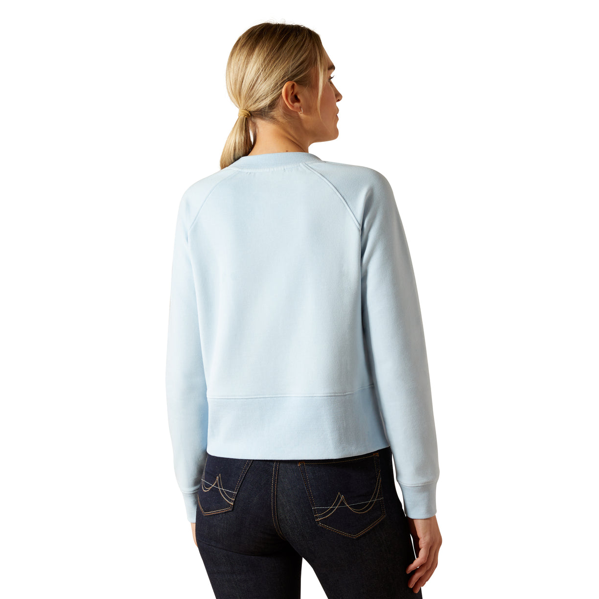 Woman wearing a light blue sweatshirt and dark jeans on a white background