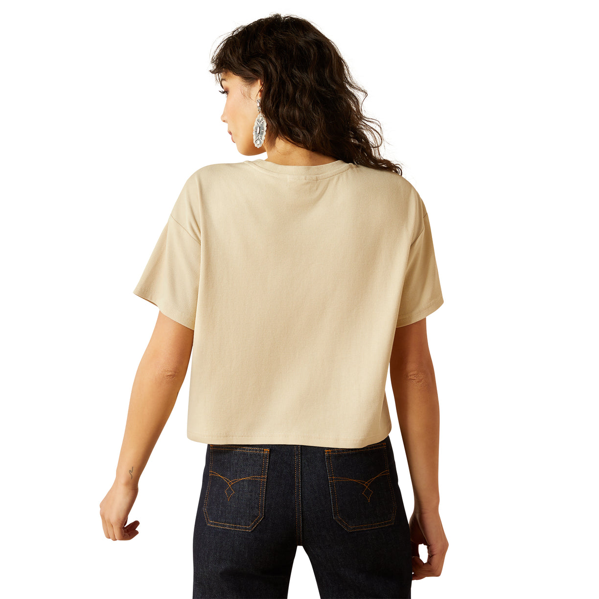 Woman wearing a beige t-shirt and dark jeans on a white background