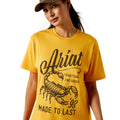 Woman wearing a yellow Ariat t-shirt with a scorpion graphic on a white background