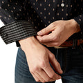 Person adjusting the cuff of a dark shirt with a subtle pattern.
