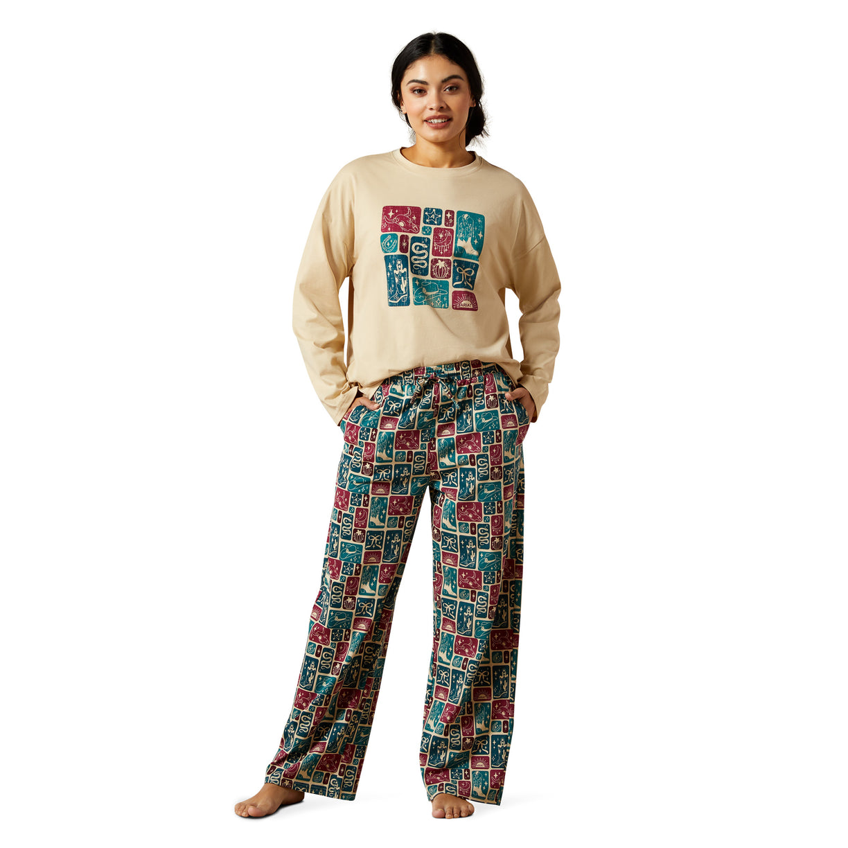 Woman wearing a beige sweatshirt with colorful graphic and patterned pants on a white background