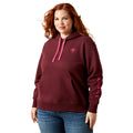 Woman wearing a maroon hoodie with pink accents and 'Ariat' branding on a white background