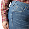 Close-up of blue jeans with a plaid shirt worn underneath on a white background