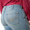 Close-up of blue jeans with a brand logo on the pocket, worn by a person in a red shirt.