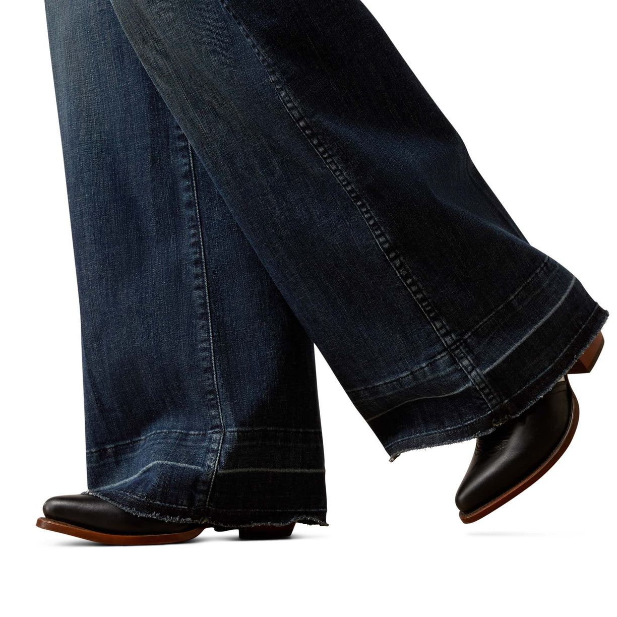 Close-up of dark blue jeans with a slight roll at the hem, paired with black shoes on a white background.