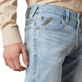 Close-up of light blue jeans with a brand logo, worn by a person.