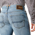 Person wearing blue jeans with an Ariat logo on a white background