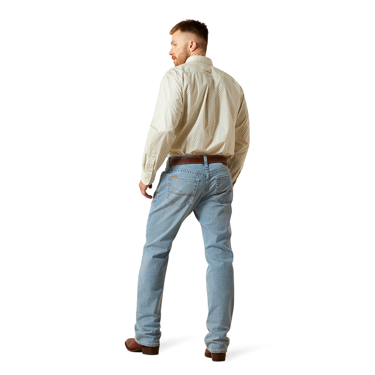 Man wearing a patterned shirt and light blue jeans on a white background