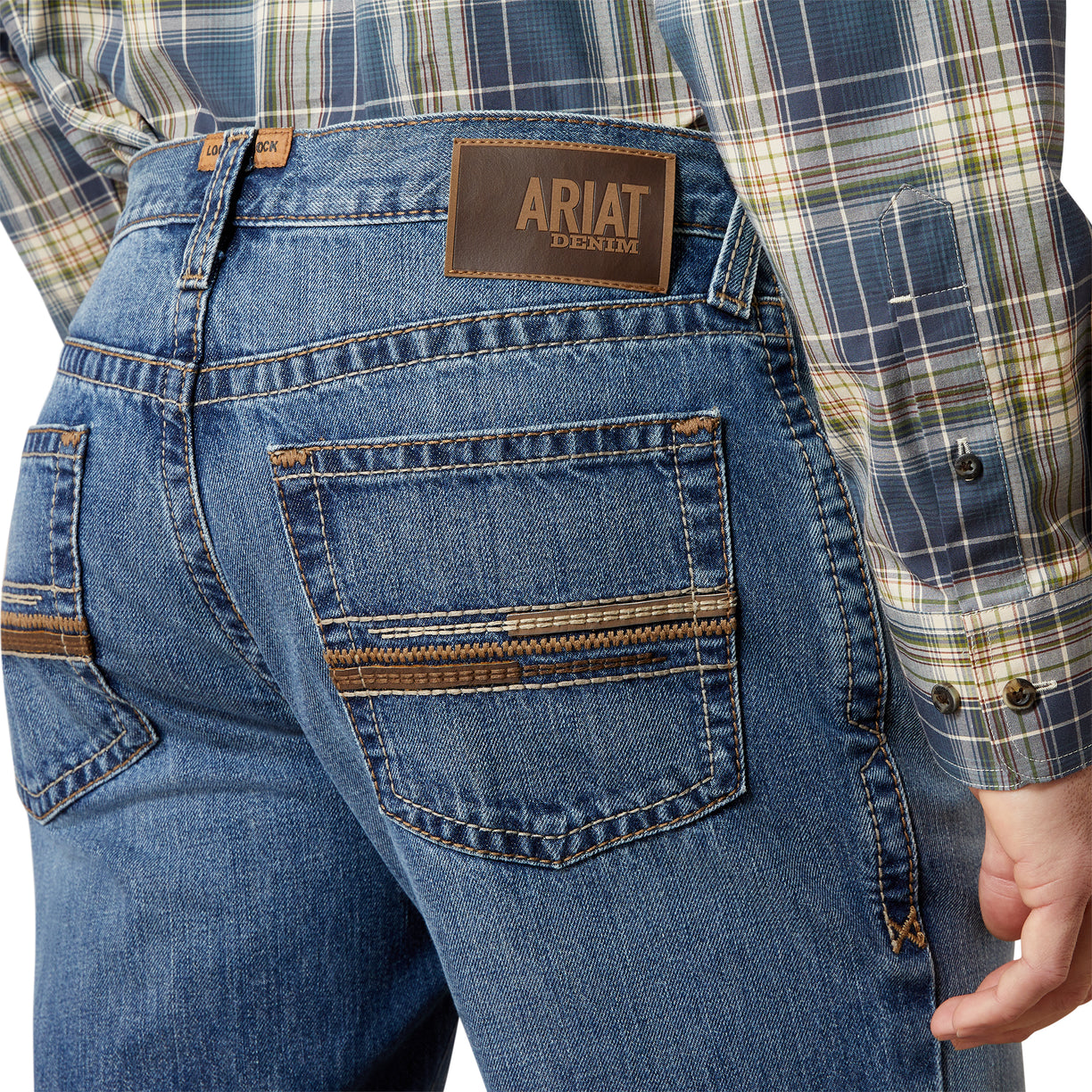 Close-up of blue jeans with Ariat denim label and plaid shirt.