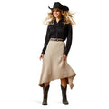 Woman wearing a black cowboy hat, black shirt, beige skirt, and brown boots on a white background