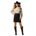 Woman wearing a beige sweater with floral designs, black skirt, and cowboy hat on a white background