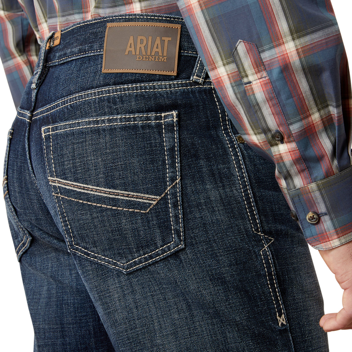 Close-up of blue jeans with Ariat branding, worn with a plaid shirt.