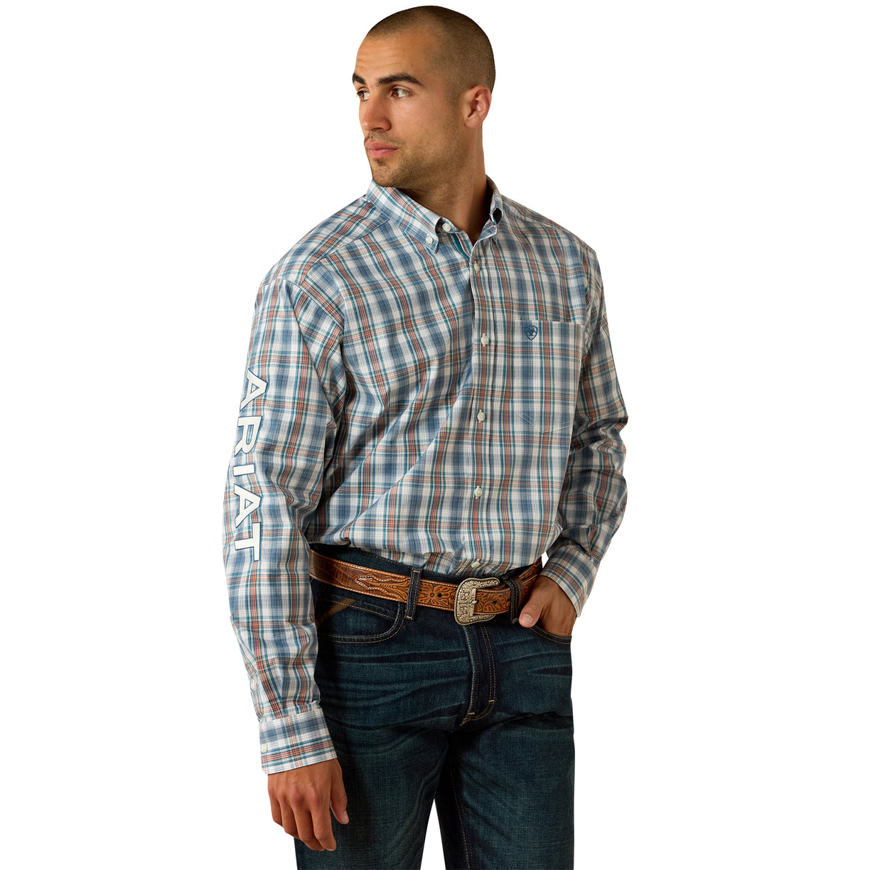 A man wearing a long-sleeve plaid button-down shirt in blue, white, and brown, paired with dark blue jeans and a brown leather belt. The shirt features the brand name 'ARIAT' printed vertically in white on the left sleeve.