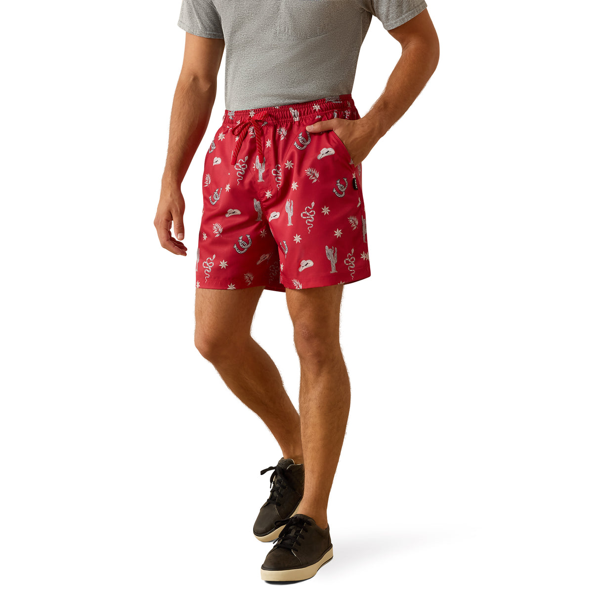 A man wearing red drawstring shorts with a white printed pattern, paired with a gray t-shirt and black sneakers, shown from the waist down on a white background.