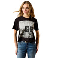 A woman modeling a black short-sleeve graphic t-shirt with a distressed black-and-white print of road signs, paired with blue jeans, against a plain white background.