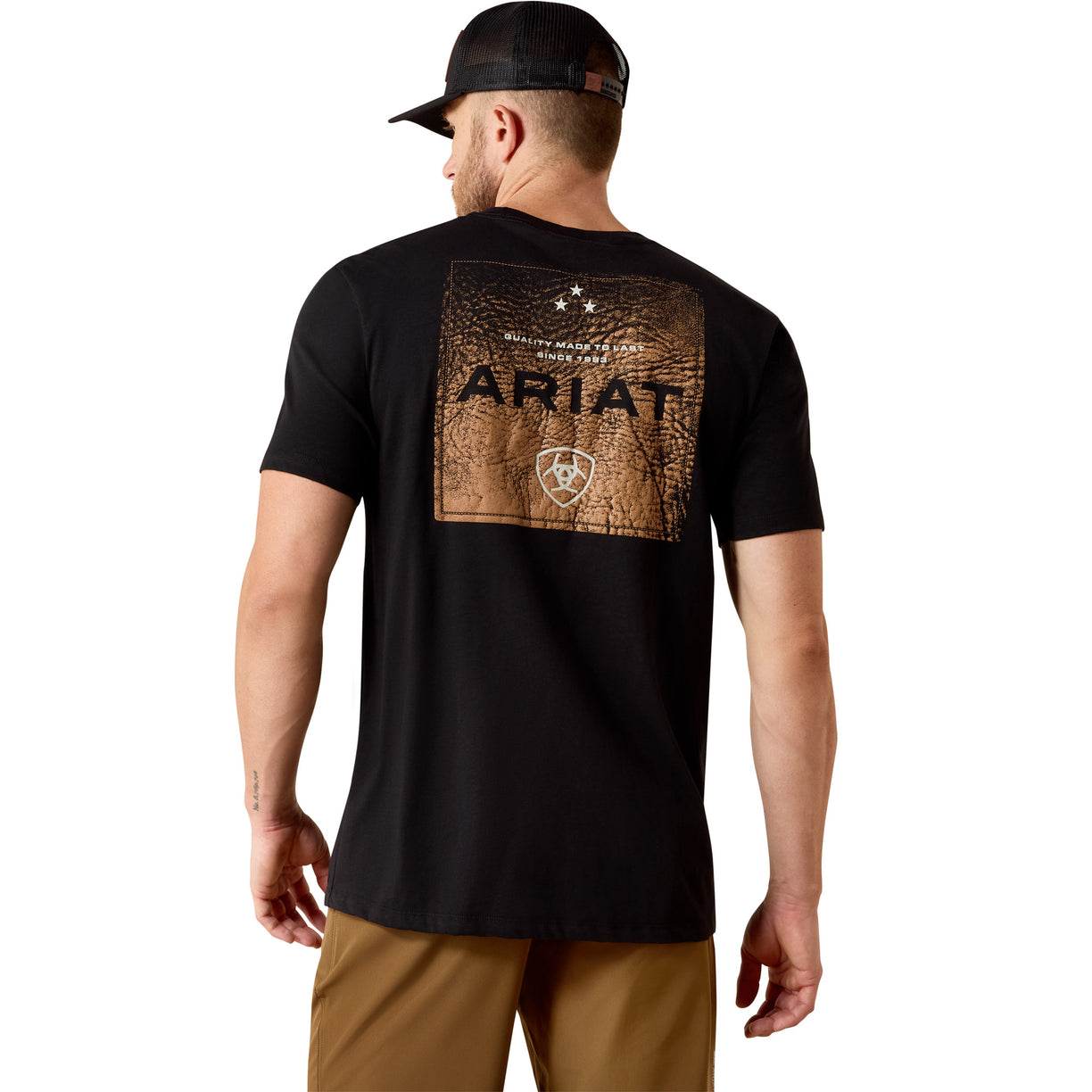 Person wearing a black Ariat t-shirt with branding on the back, standing against a white background.