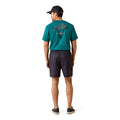 A man shown from the back wearing a teal short-sleeve t-shirt with a graphic on the back, dark charcoal shorts, and a black baseball cap, standing against a plain white background.