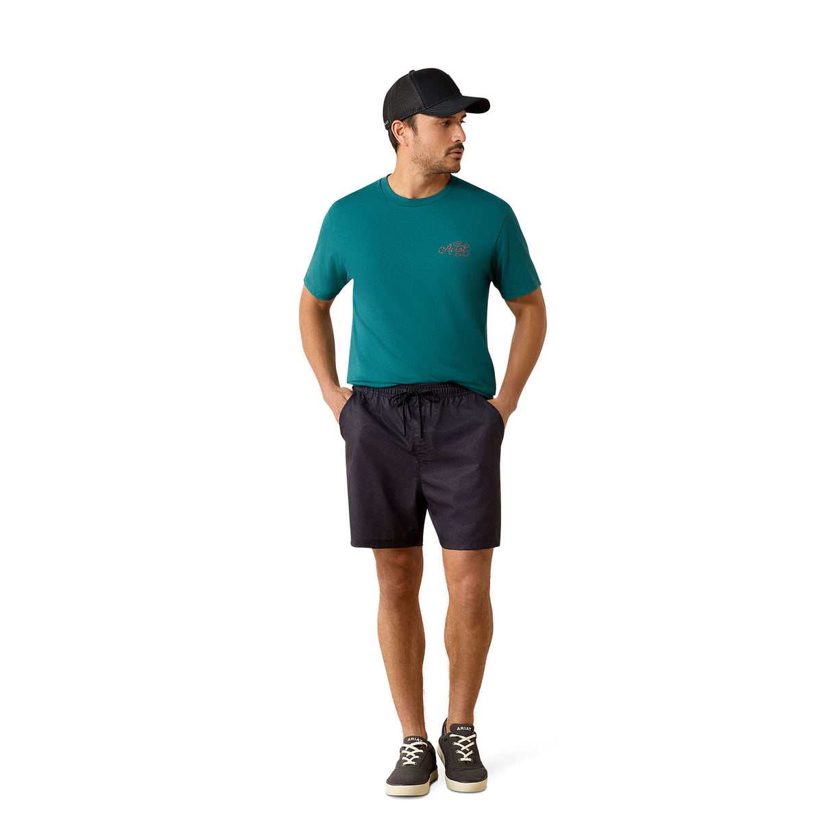 A man wearing a teal short-sleeve athletic t-shirt, dark charcoal drawstring shorts, a black baseball cap, and black sneakers, standing against a solid white background.