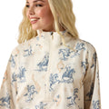 Woman wearing a cream-colored jacket with blue horse and rider pattern on a white background